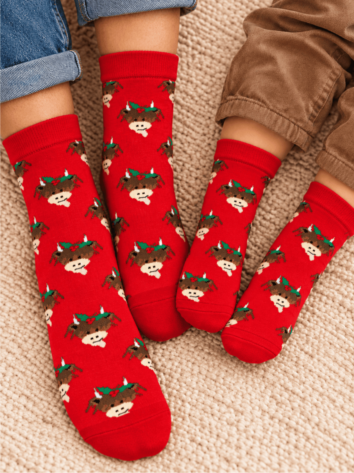 Hamish Christmas Socks worn by an adult and a child together, red with Hamish the Highland Cow in his Christmas holly